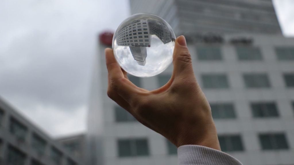 Eine Hand hält eine Glaskuel, darin spiegelt sich ein Gebäude