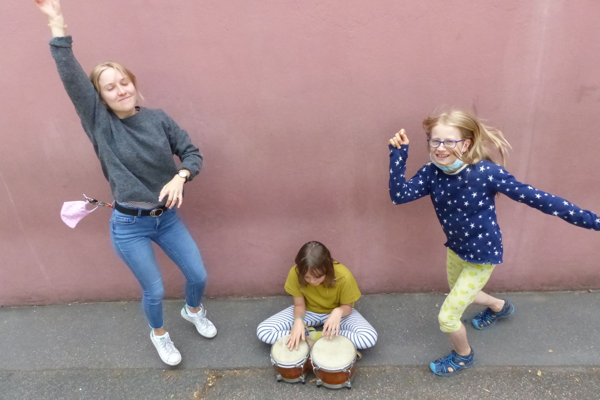 Drei Mädchen, zwei tanzen rechts und links neben einem Mädchen, das trommelt