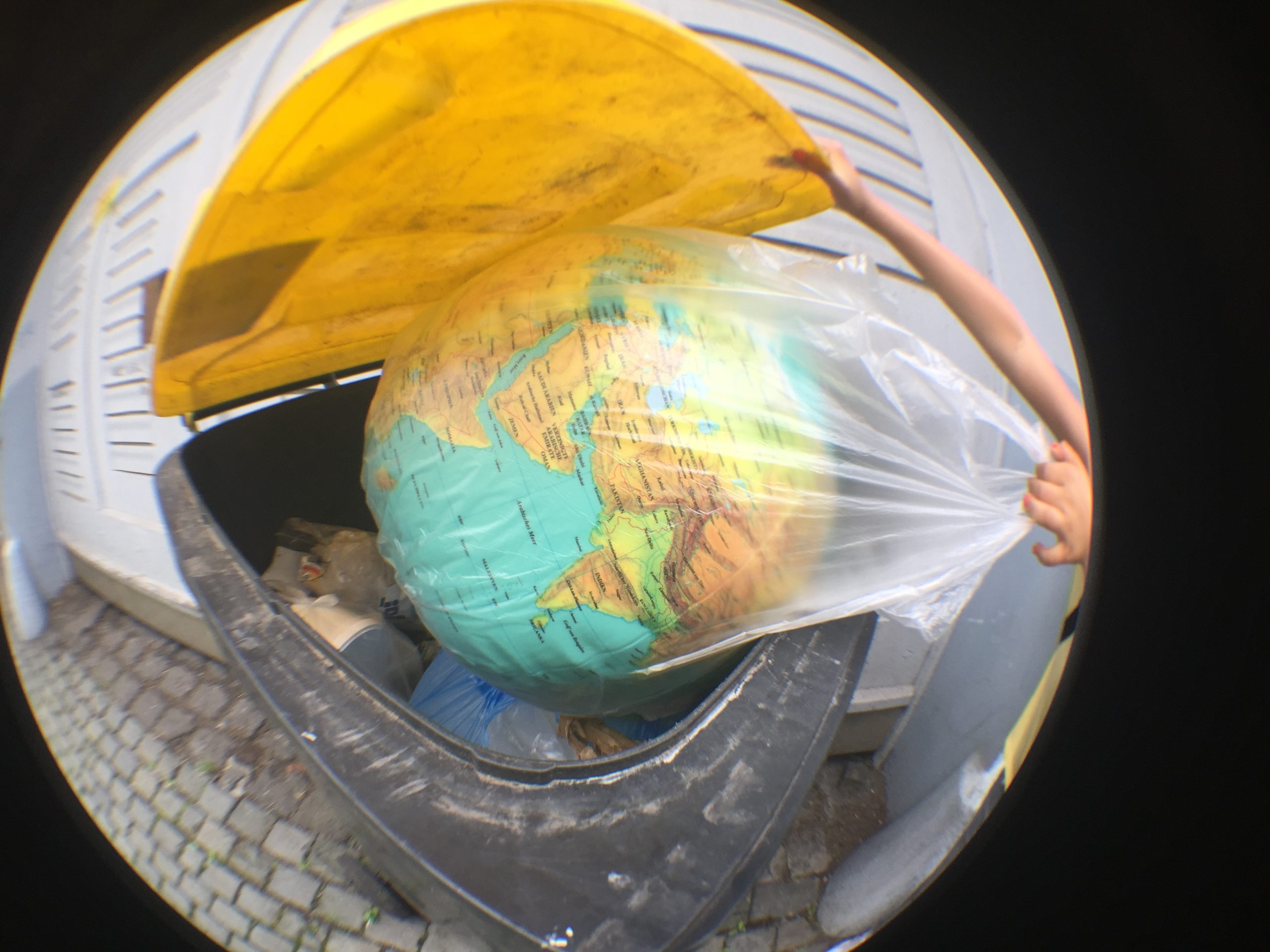 ein Globus, in einem durchsichtigen Müllbeutel wird in eine Mülltonne geworfen