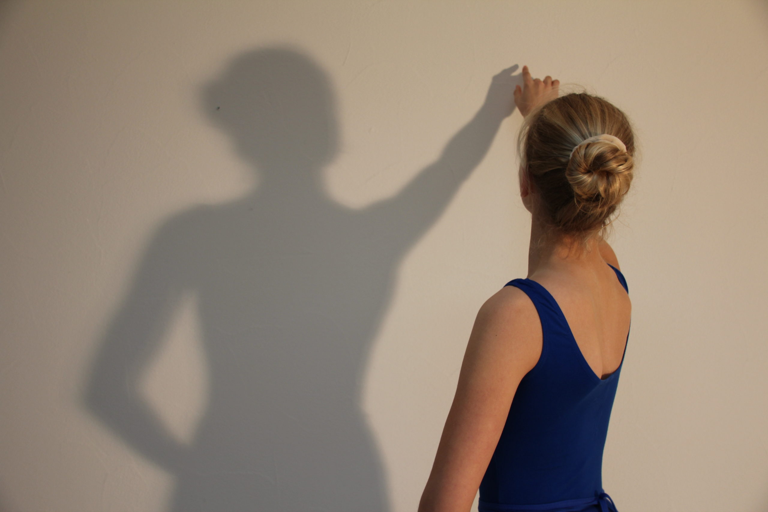 ein Mädchen im Kleid berührt ihren Schatten an der Wand